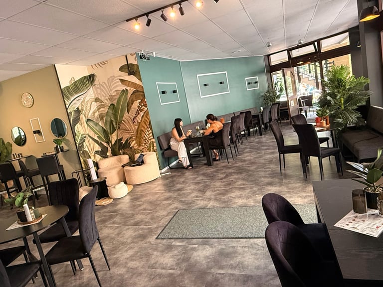 Modern office or salon space with black chairs, potted plants, light fixtures, and teal accent wall with seated clients and staff